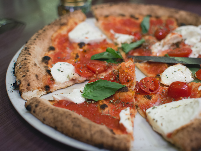 Italian inspired pizza topped with fresh basil leaves and tomatoes on a true mozzarella cheese and pepperoni.