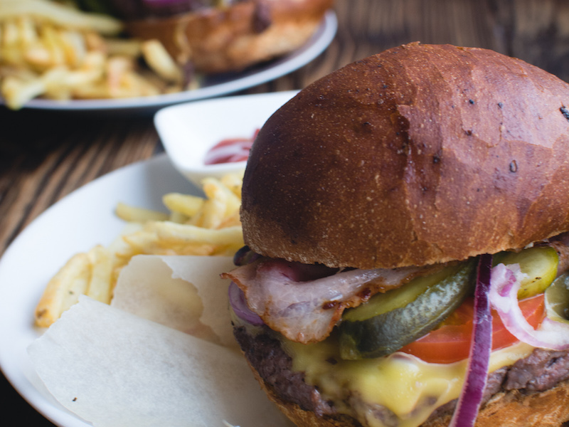 Grilled gourmet burger topped with cheddar cheese and oven baked bacon.